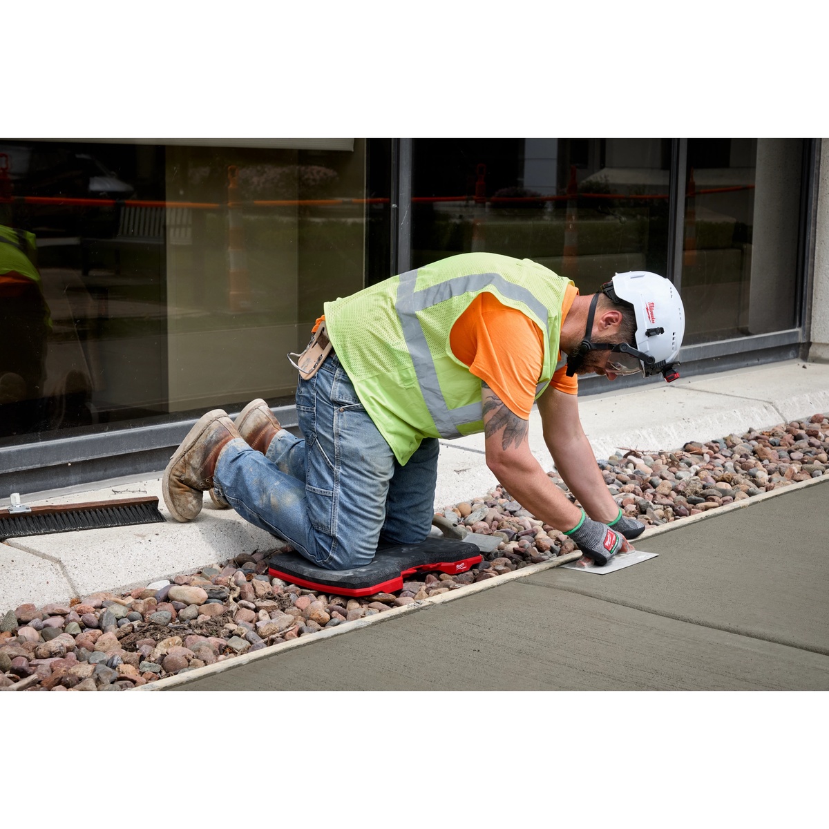 Milwaukee 48-73-6110 PACKOUT Kneeling Pad supporting a worker finishing wet concrete beside a building walkway on a jobsite