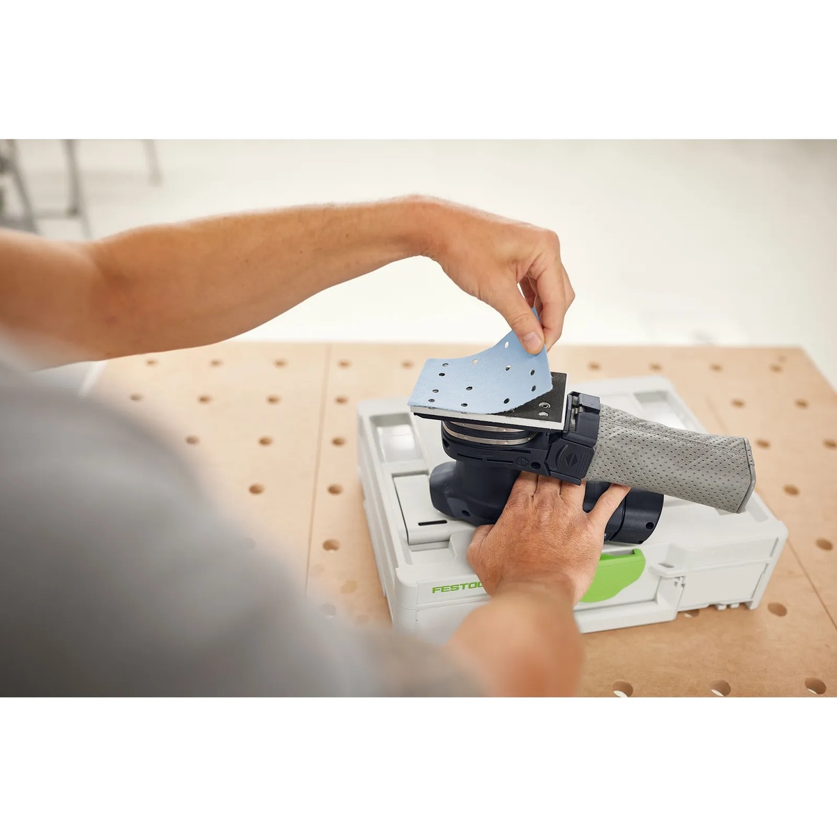 Festool 578194 Granat RTS/RTSC/LS130 80x133 Abrasives 100-Piece Value Set Systainer3 abrasive sheet being installed on a compatible Festool sheet sander on a perforated workbench