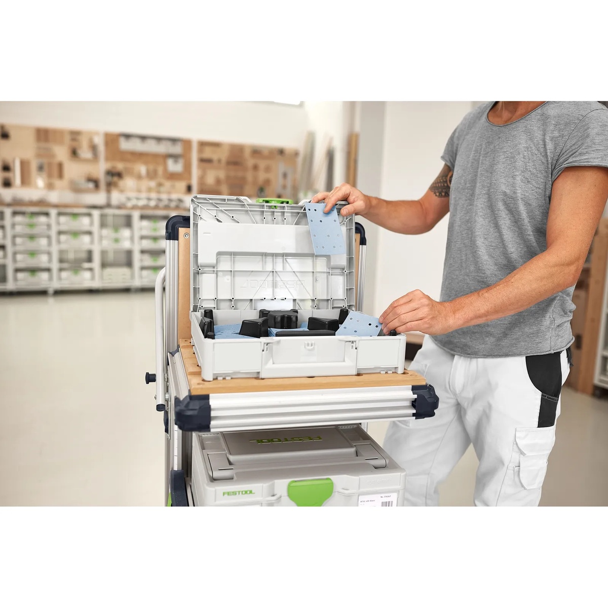 Festool abrasives Systainer on a rolling jobsite cart with a user pulling 80x133 sanding sheets for finishing work in a workshop