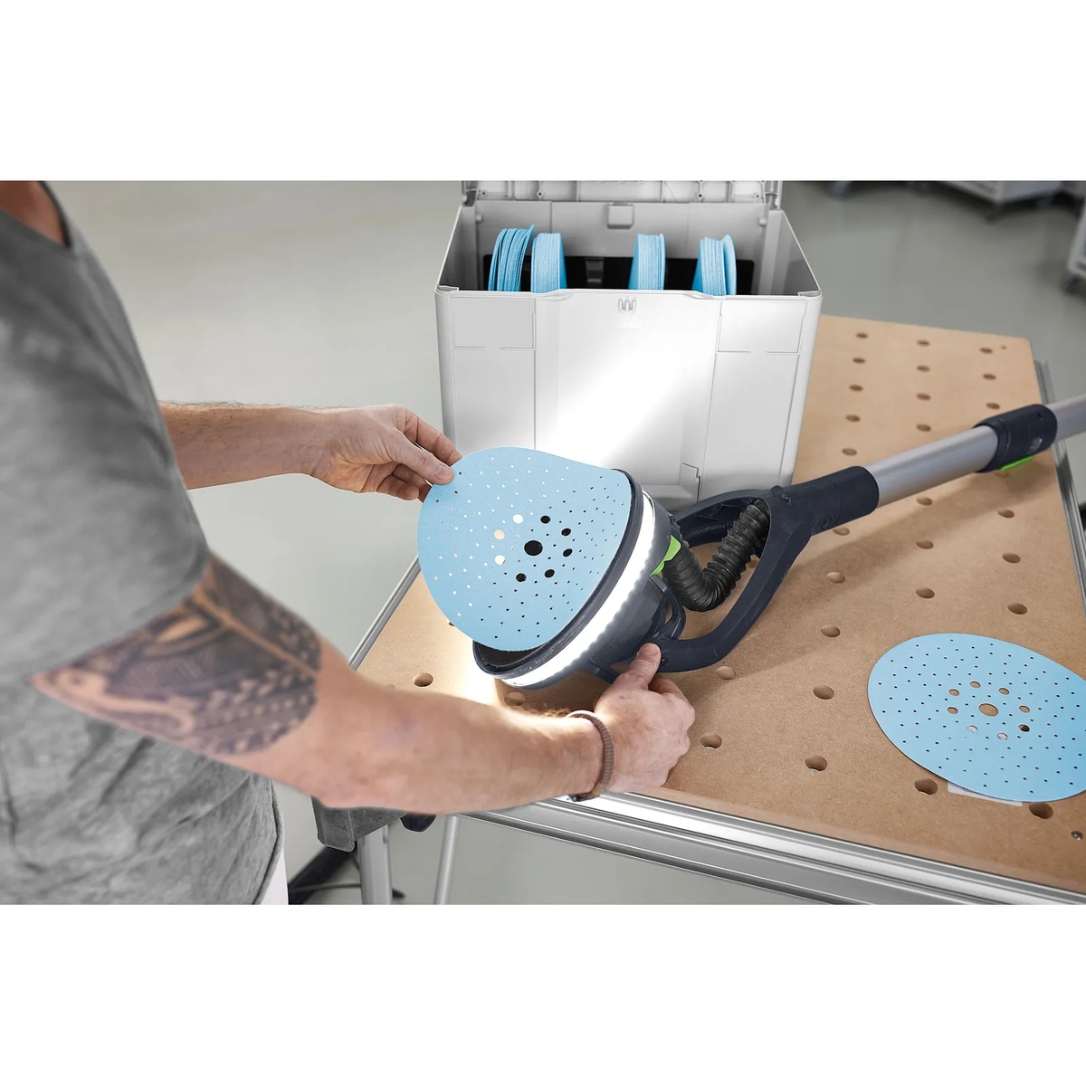 Festool 578281 D225 GR SYS Granat abrasive disc being installed on a Festool PLANEX long-reach sander over a perforated worktable in a workshop