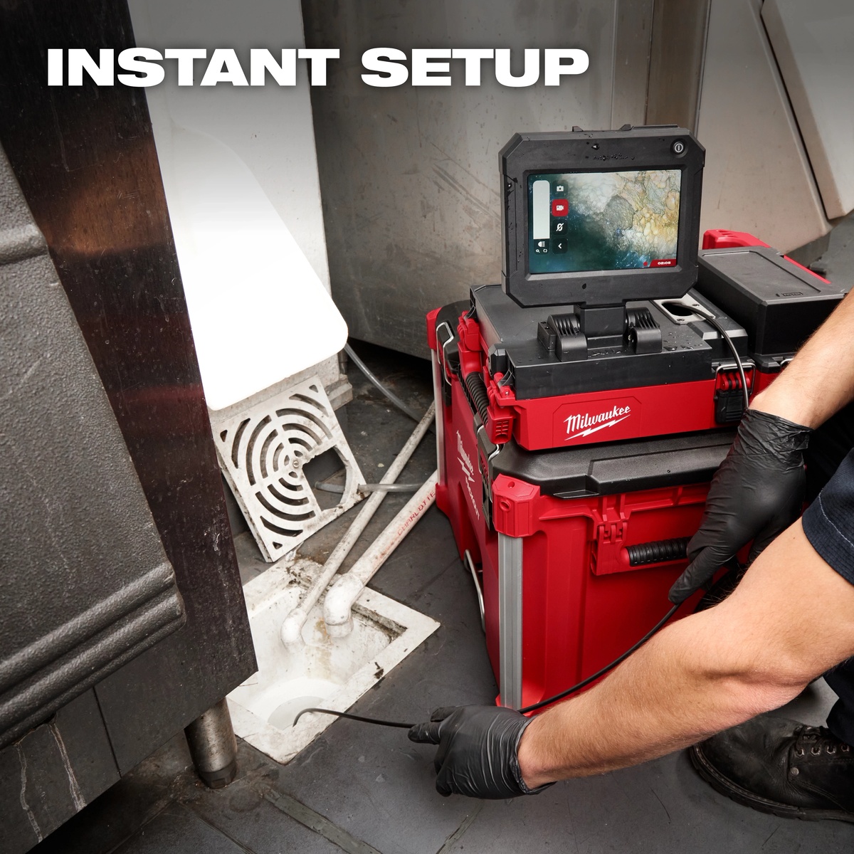 Milwaukee 3154-20 M12 75' Drain Camera w/ PACKOUT Compatibility set up at a floor drain with the adjustable 7 inch touchscreen display visible on a service call
