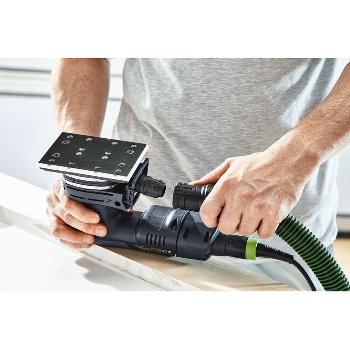 Festool RTSC 400 18V Brushless Hybrid Sander Set w/ Granat Abrasive Value Set Systainer connected to a dust extractor while sanding a wood edge on a bench in a finish work setting