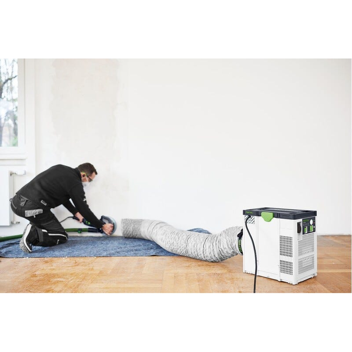 Festool SYS-AIR HEPA air filter connected to its long air supply hose across a room during interior sanding and dust control work on a renovation jobsite