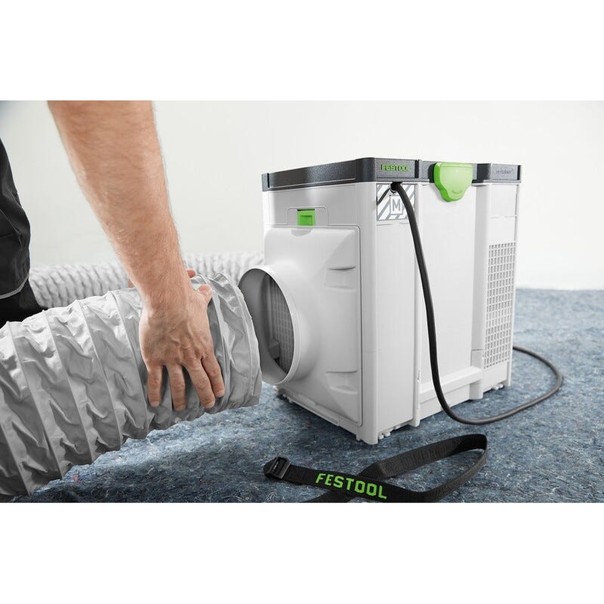 Festool SYS-AIR HEPA air filter with hose being connected in a shop setting, showing the Systainer-style body and portable setup for indoor dust filtration