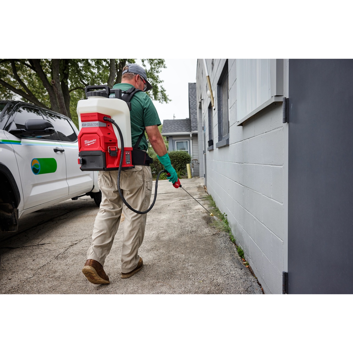 Milwaukee 49-16-19PS 4-Gallon Sprayer Tank Assembly w/ SWITCH-TANK being used outdoors along a building wall for controlled exterior liquid treatment application