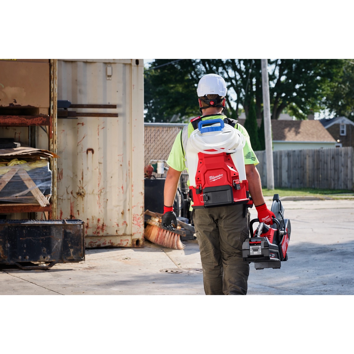 Milwaukee 3019-21WS M18 4-Gallon Water Supply Kit w/ SWITCH TANK carried as a backpack on a construction site while a worker transports a cut-off saw for concrete cutting