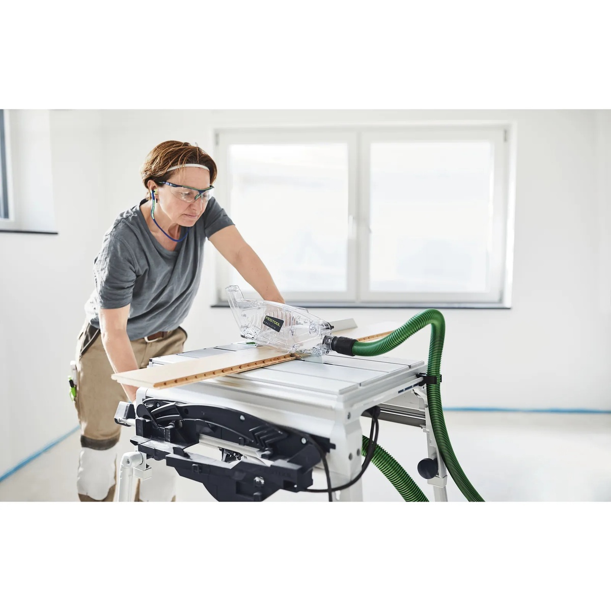 Festool dust extraction hose set in use on a bench-mounted circular saw during indoor woodworking to reduce dust around the blade guard and machine