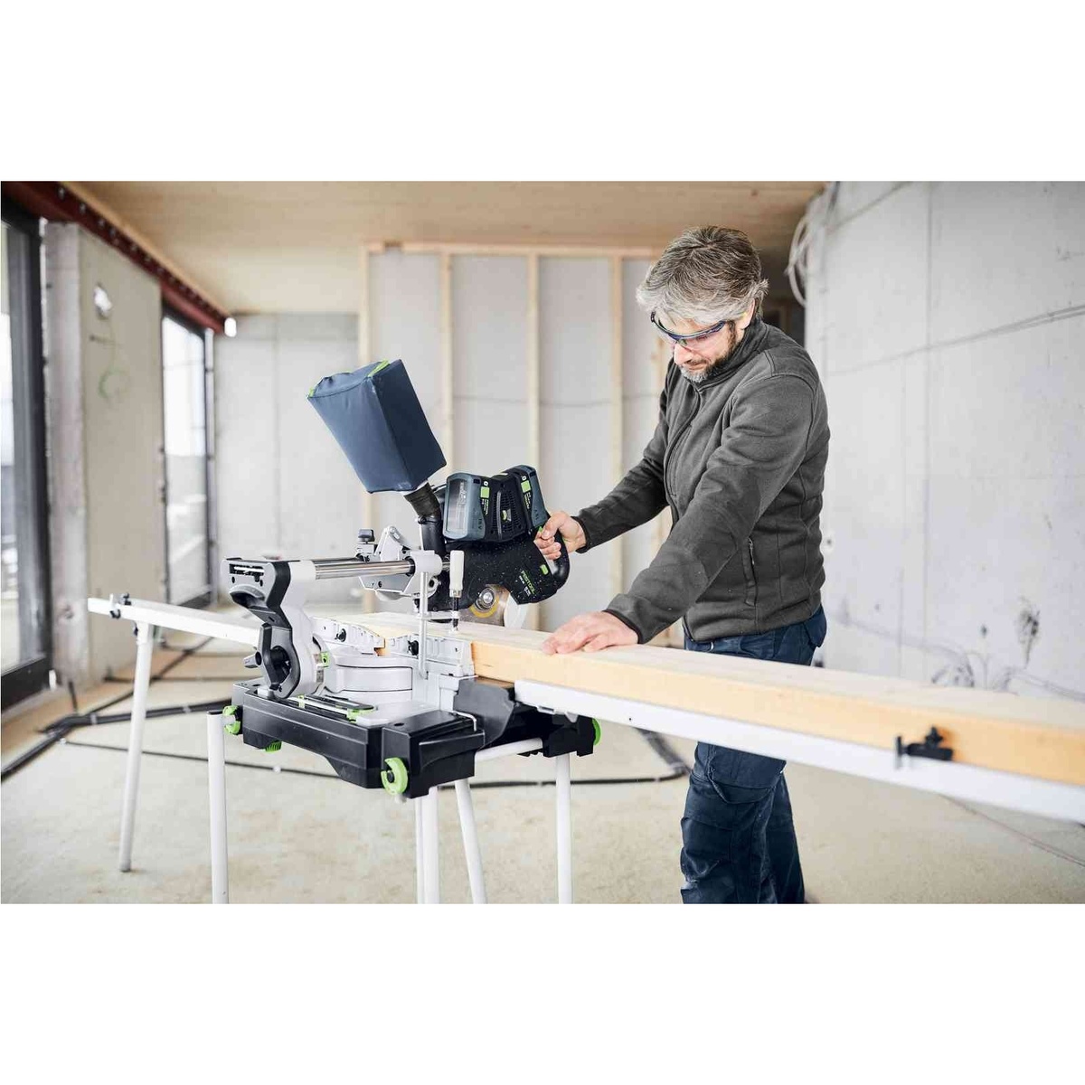 Festool 577176 Kapex KSC 60 EB Cordless Dual-18V Miter Saw 5.0 Kit cutting long lumber on a mobile stand inside a framing and finish jobsite