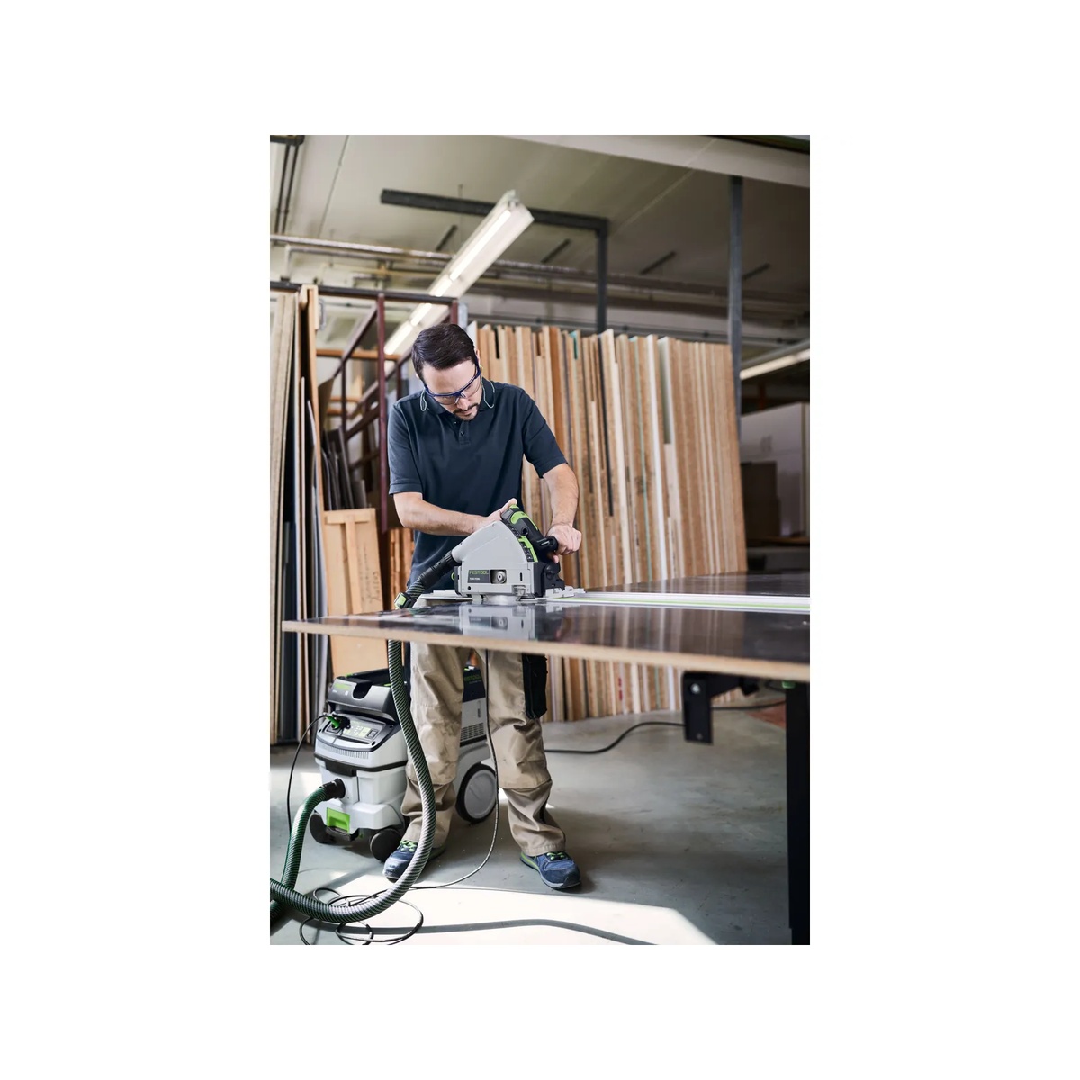 Festool 577871 CLEANTEC CT 26 EI HEPA Dust Extractor rolling beside a user cutting sheet material in a woodworking shop