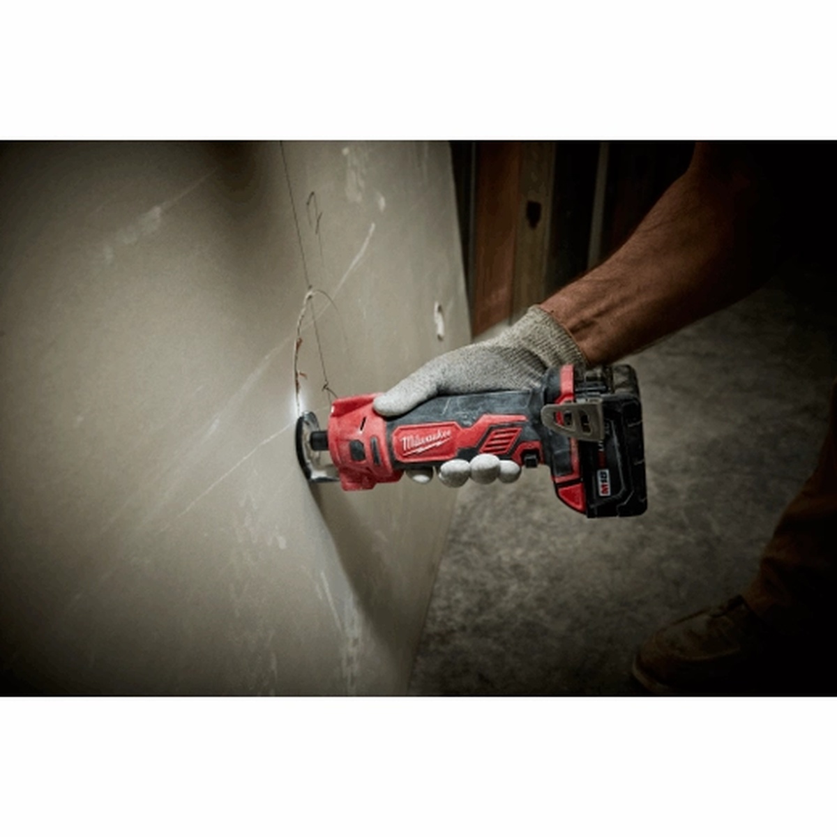 Milwaukee 2627-20 M18 Cut Out Tool cutting a drywall wall opening on a jobsite during remodel work