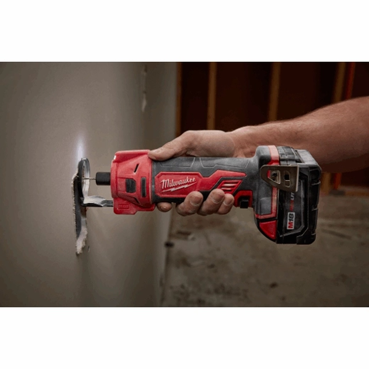 Milwaukee 2627-20 M18 Cut Out Tool making a drywall cut around a wall opening in a dim indoor work area