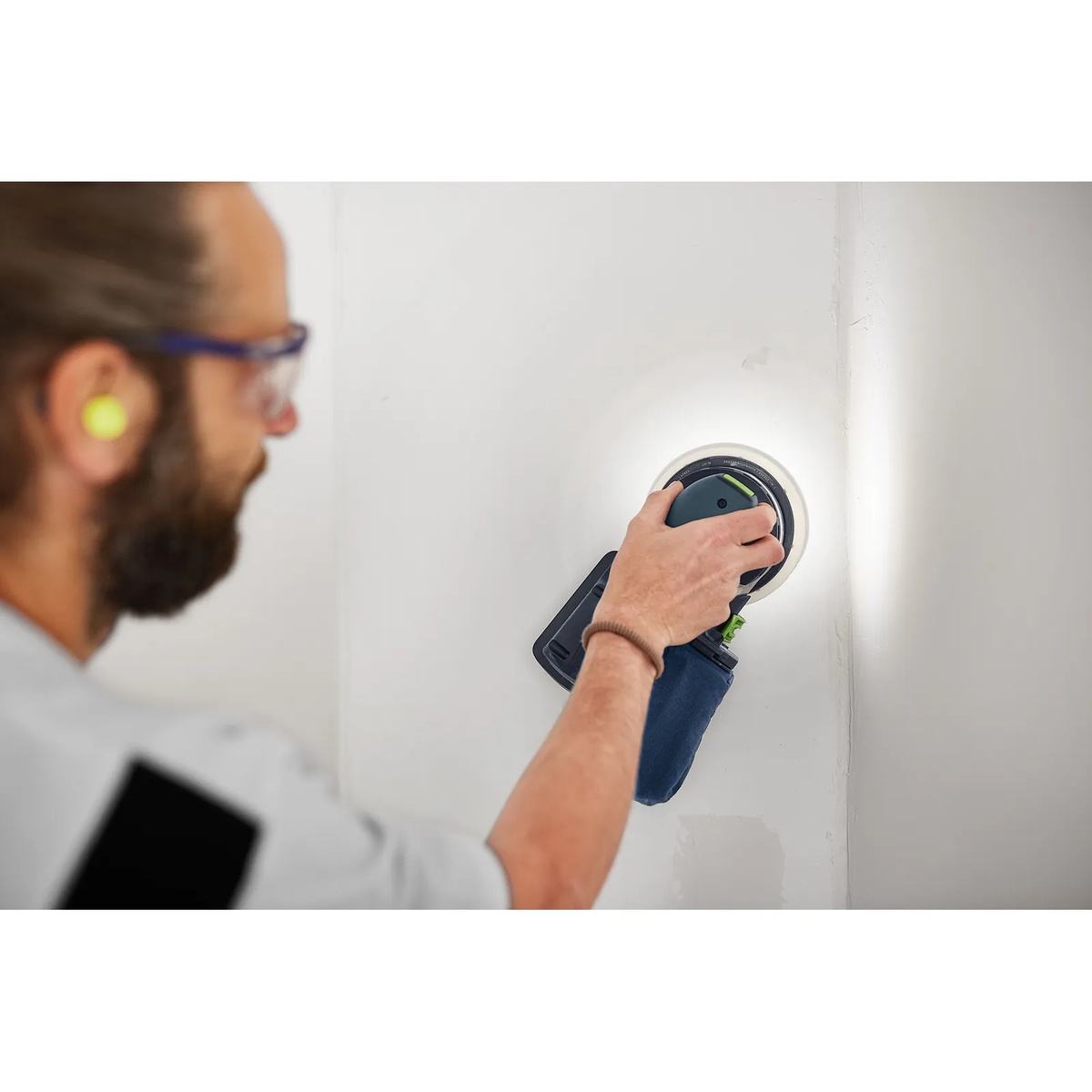 Festool ETSC 2 150 4,0 I-Plus cordless random orbit sander sanding a vertical wall surface indoors with the integrated light ring highlighting uneven areas during finish prep
