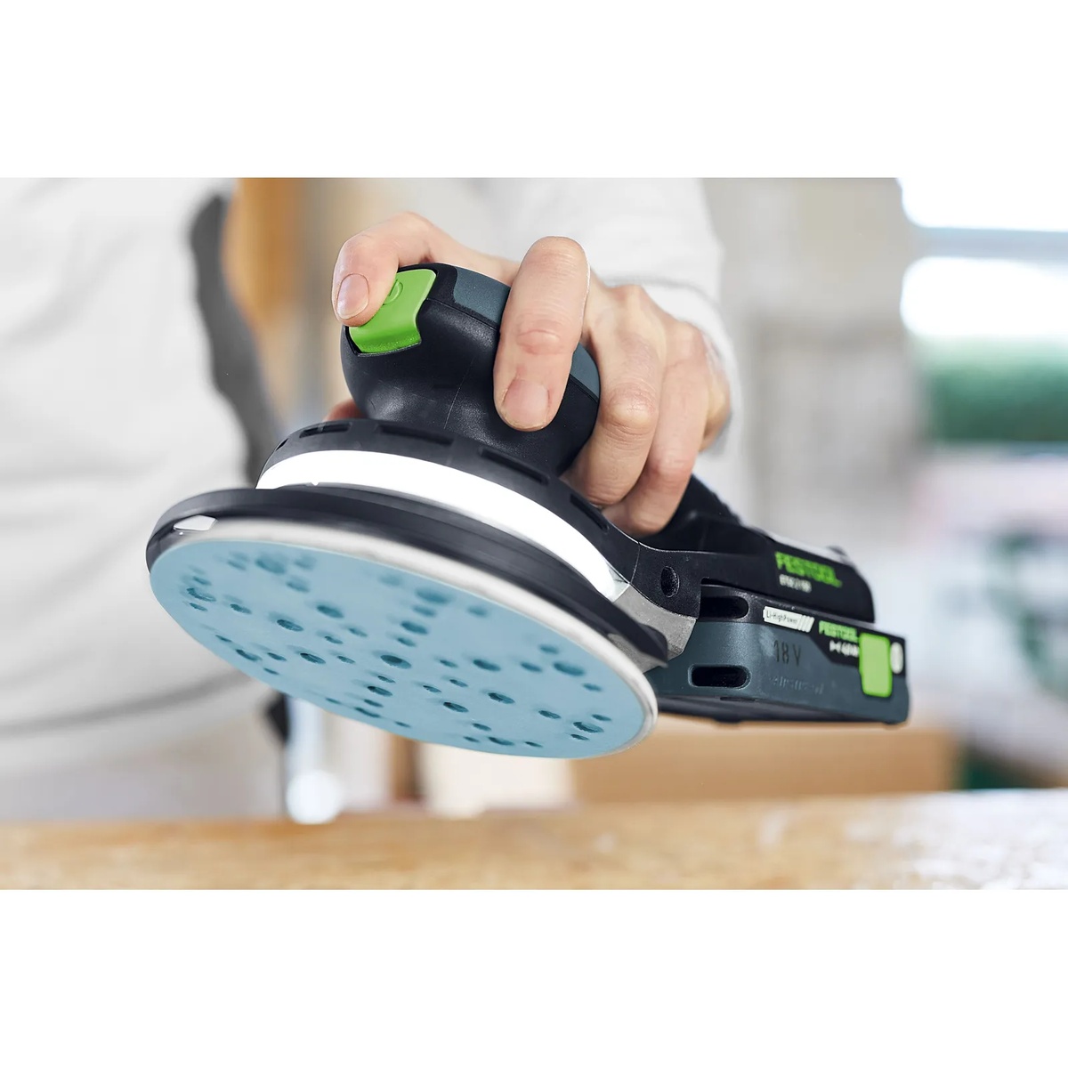 Festool ETSC 2 150 4,0 I-Plus cordless random orbit sander shown close up in hand over a wood workbench, highlighting the low-profile body and 6 inch sanding pad