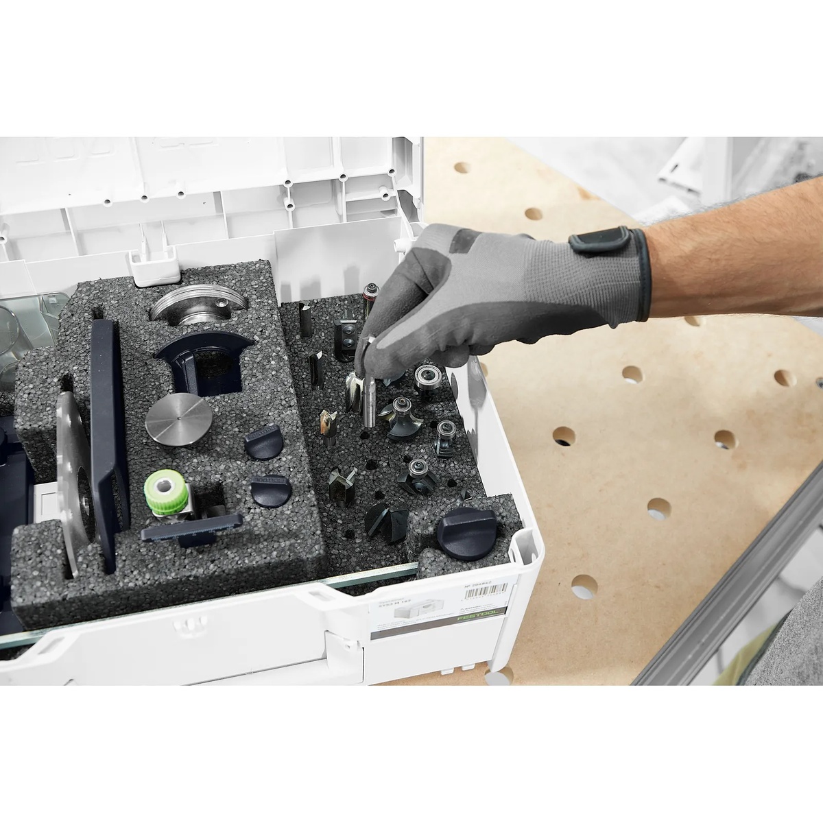 Festool 578047 ZS-OF 1010 I 17-Piece Imperial Router Accessory SYS3 Set with router bits and accessories organized in foam while a gloved hand selects a cutter at a workbench