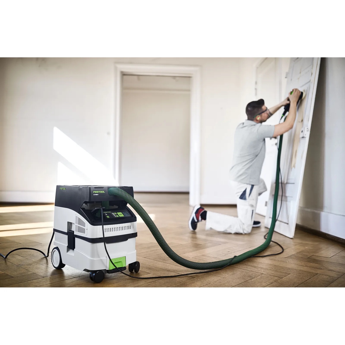 Festool CT MIDI I HEPA Bluetooth Dust Extractor collecting dust while a contractor sands a door indoors during prep and finishing work