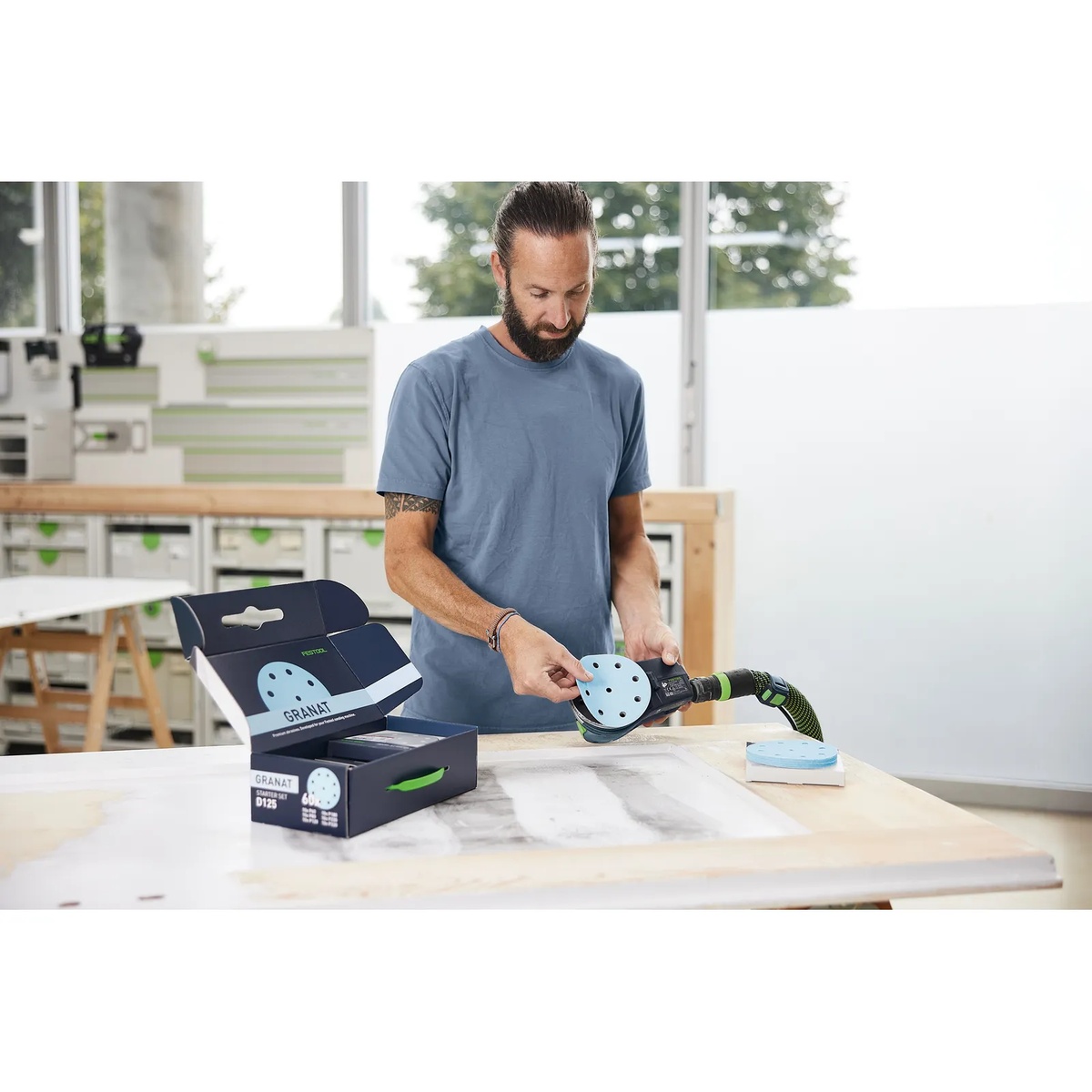 Compatible Festool random orbit sander being fitted with a Festool D125 GR-Set sanding disc at a woodworking bench