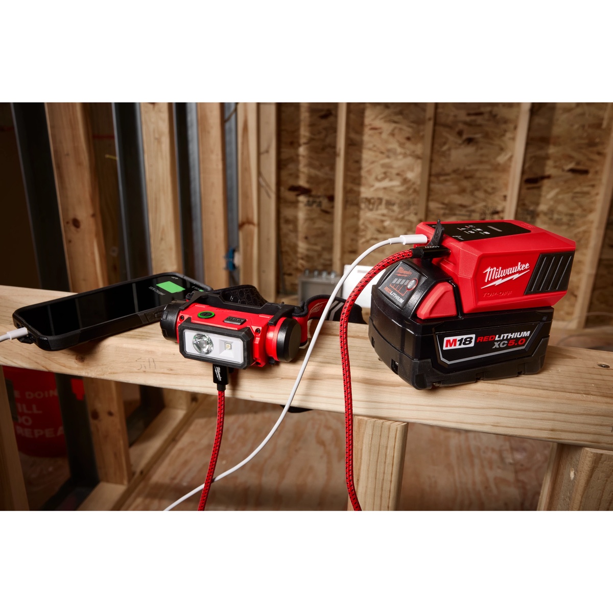 Milwaukee 2847-20 M18 TOP-OFF Charger & Power Supply powering jobsite electronics and a work light from an M18 battery on a framed construction site