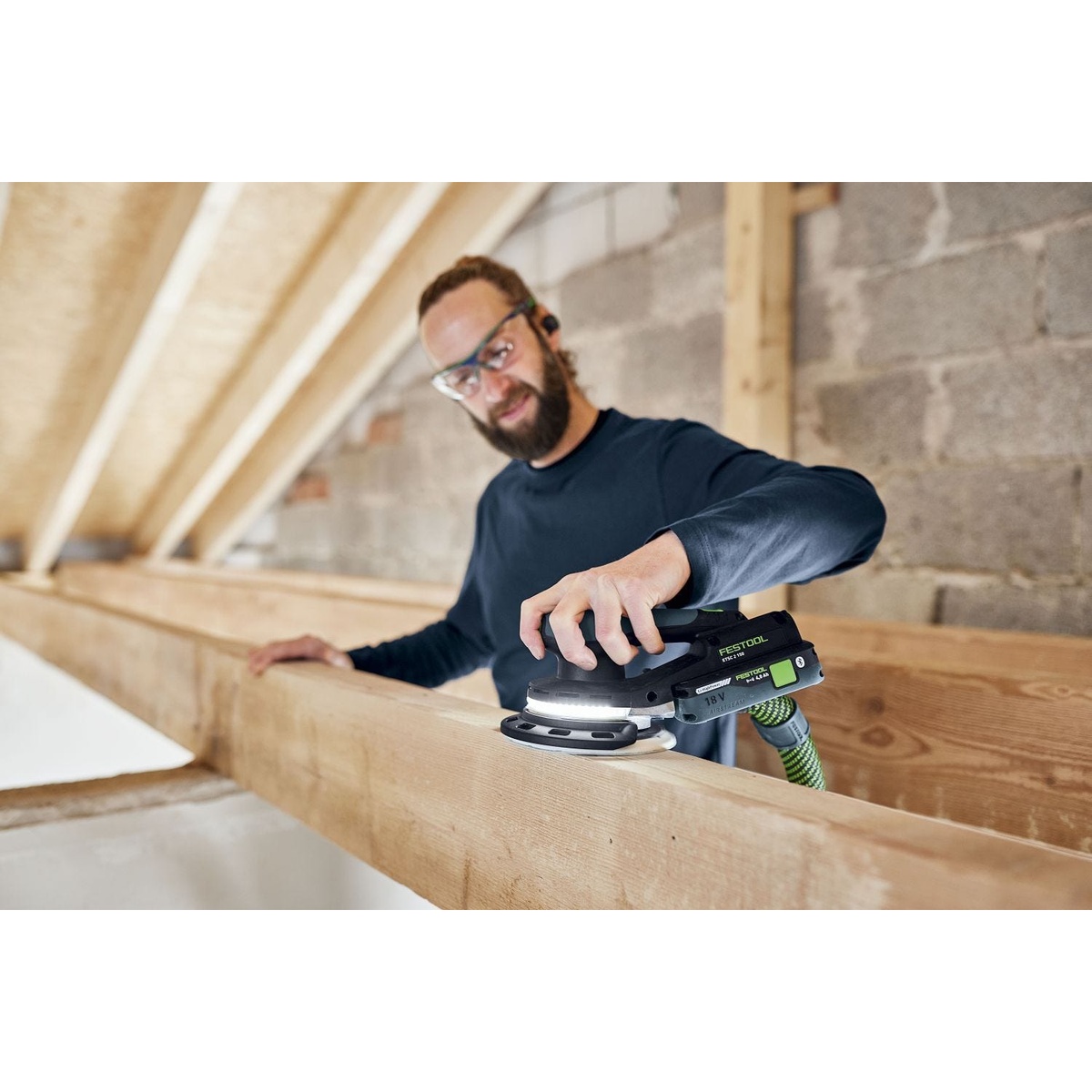 Festool Cordless 18V ETSC 2 150mm (6-in.) Sander Kit w/ 120-Piece GRANAT Abrasive Systainer Set sanding a wood beam in a framing interior with the LED light ring illuminating the surface