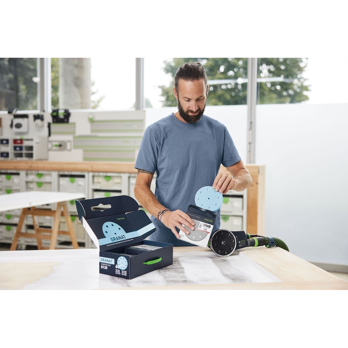 Festool Cordless 18V ETSC 2 125mm (5-in.) Sander Kit w/ 60-Piece GRANAT Abrasive Starter Pack shown with sanding discs and sander at a workbench during finish sanding setup in a woodworking shop