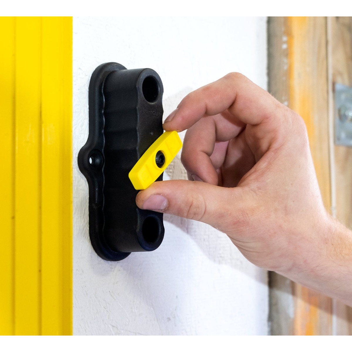 Fastcap Level Rack for Updated Stabila Level Handles mounted on a wall while a user turns the yellow cam-lock during installation in a work area