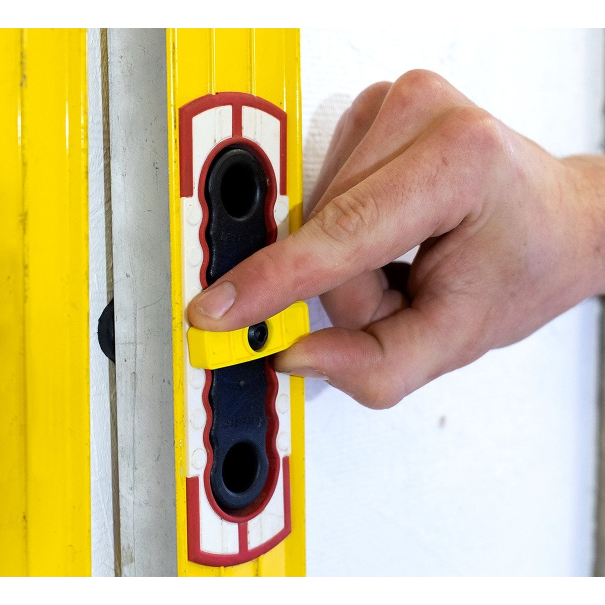 Fastcap Level Rack for Updated Stabila Level Handles securing a yellow Stabila level against a wall with the cam-lock engaged in a workshop setting
