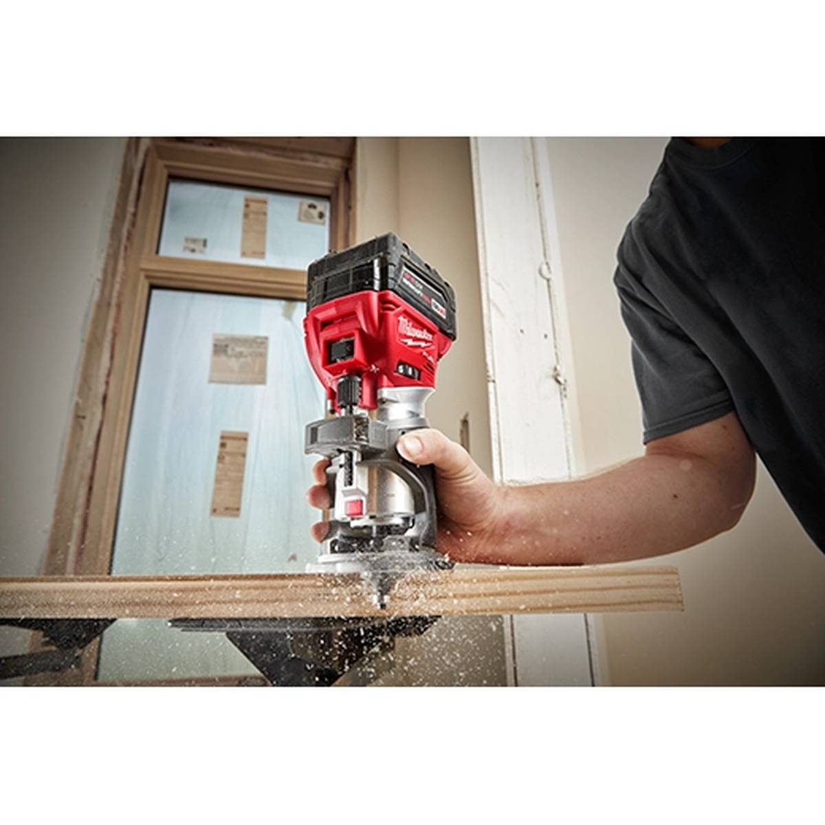 Milwaukee 2723-20 M18 FUEL Compact Router cutting the edge of a wood board during trim routing work on an indoor jobsite