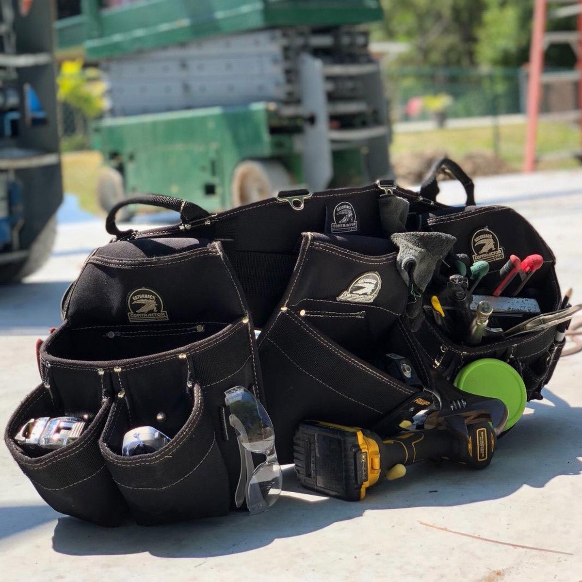 Gatorback B145 Professional Carpenters Triple Combo loaded with hand tools and fasteners on a jobsite slab near lift equipment, showing real-world carpenter carry and organization