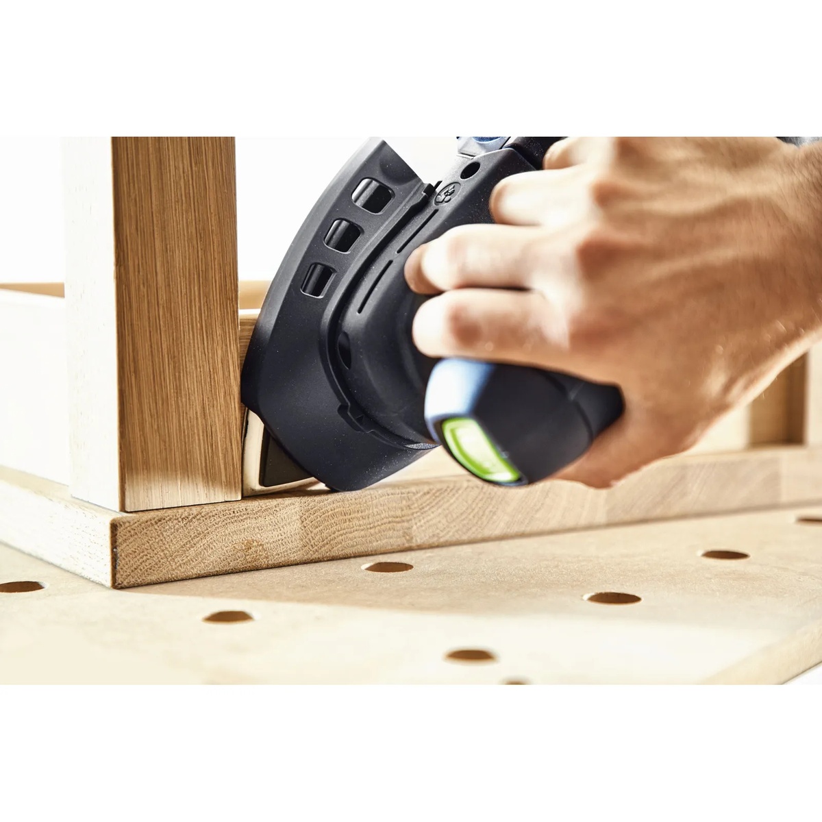 Festool delta abrasive sheet sanding a tight inside wood corner on trim work at a workbench