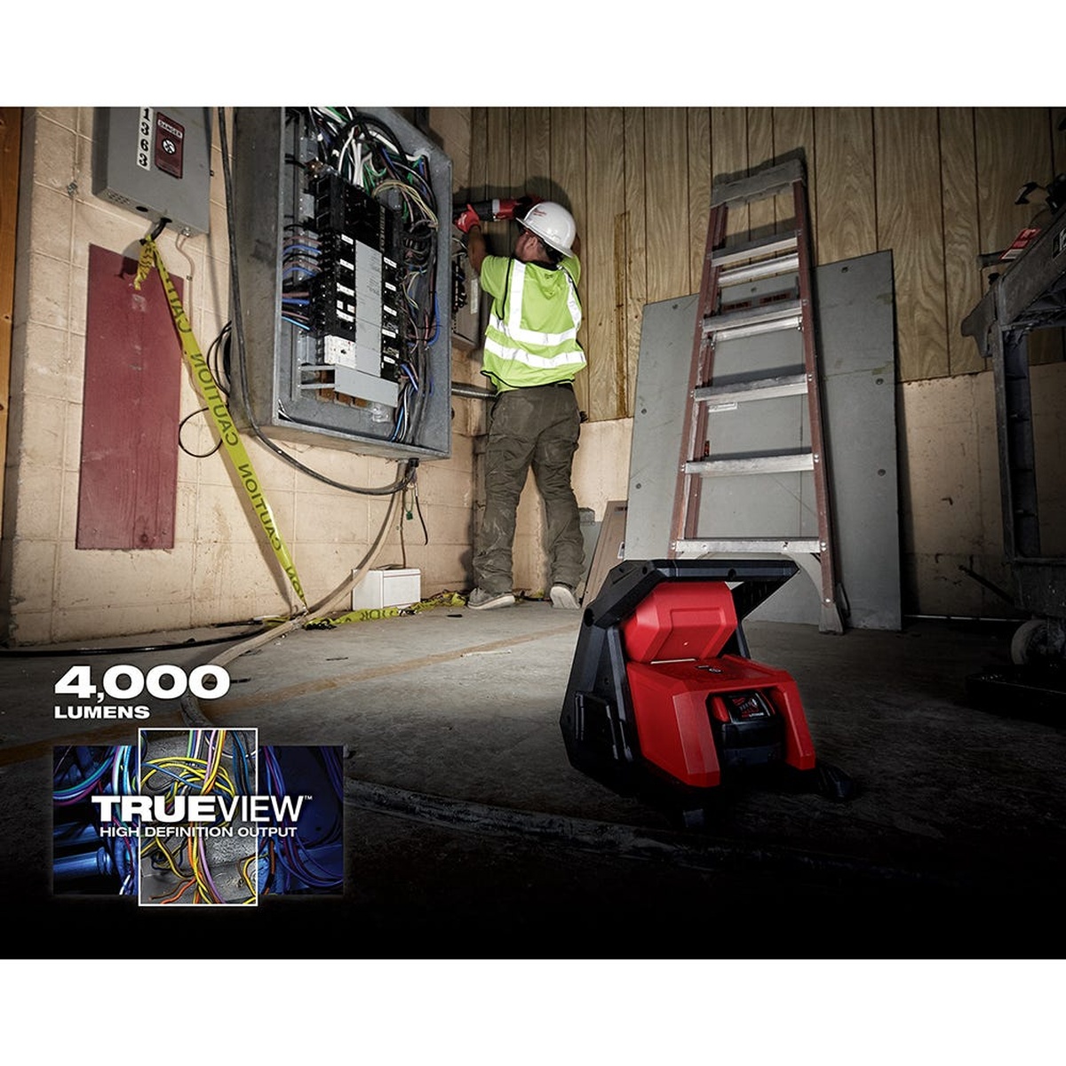 Milwaukee M18 ROVER Dual Power Flood Light + 5.0Ah Battery 2-Pack lighting an electrical work area while a technician works on a panel inside a jobsite room