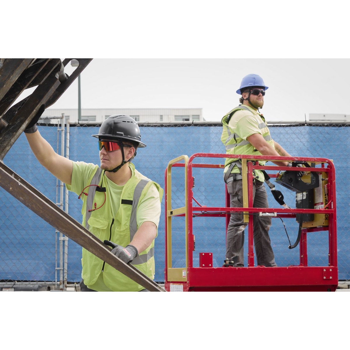 Milwaukee 48-73-2506 wrap around safety glasses worn on an outdoor construction site while workers handle steel from a lift
