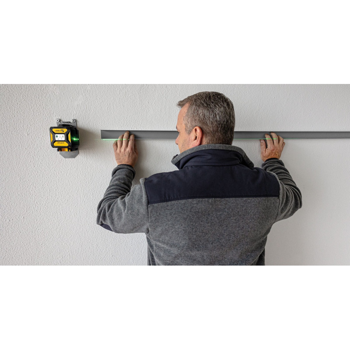 Stabila Cross line plus plumb dot laser LAX 320 G projecting a green level line on an interior wall while aligning a straightedge