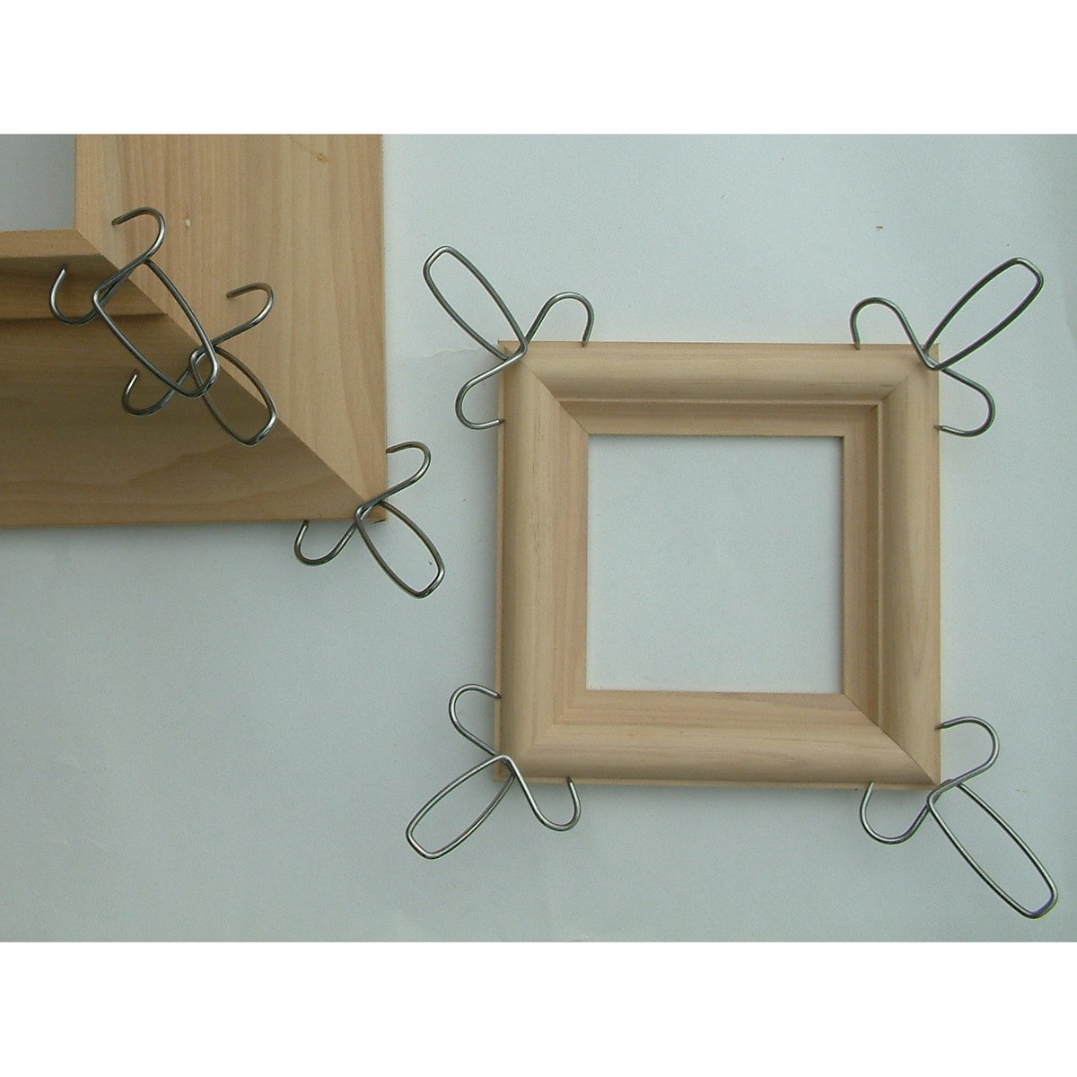 Collins 13-Pack of Miter Clamps & Pliers Kit miter clamps holding wood frame corners closed during glue-up on a workshop assembly surface