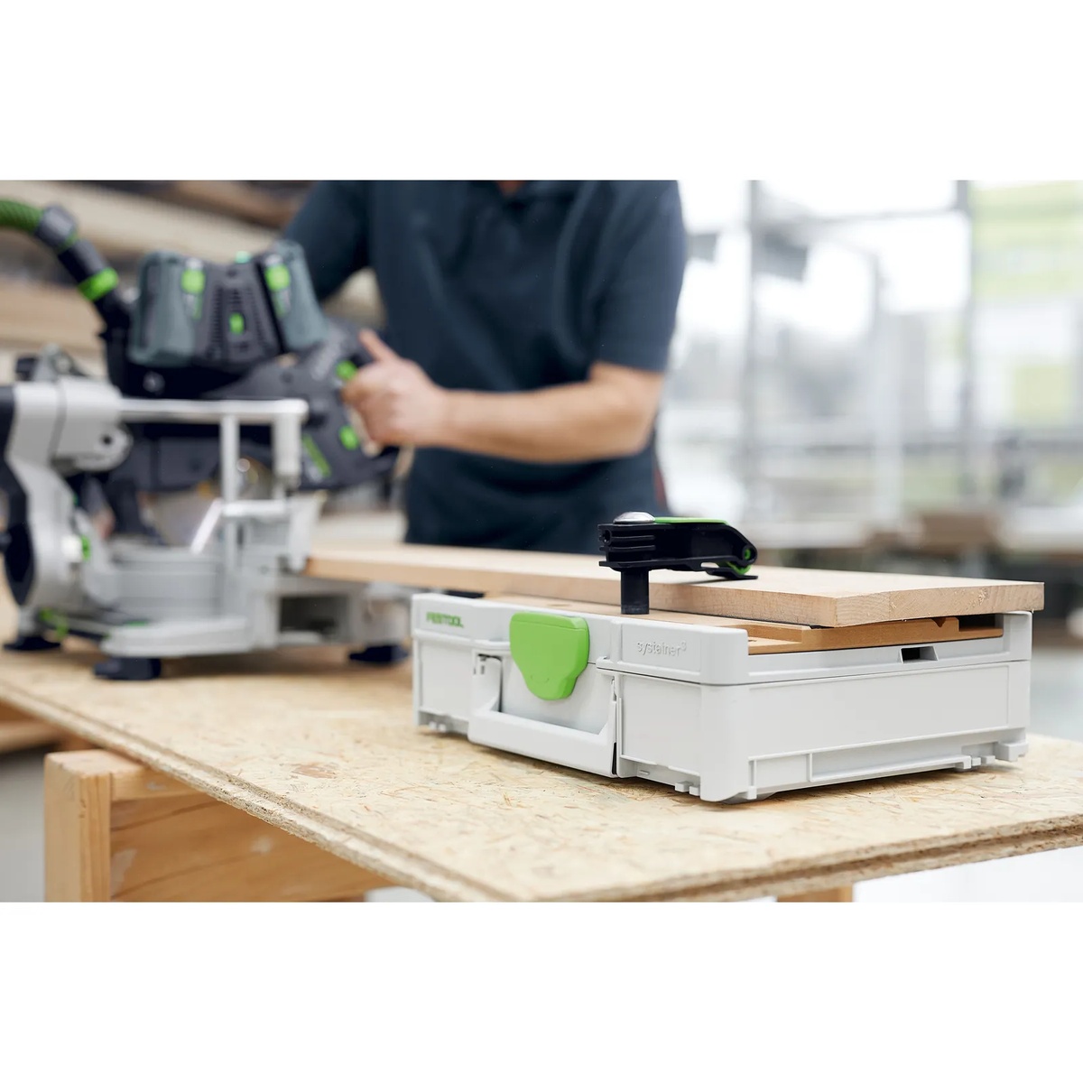 Festool portable workbench Systainer holding a wood board with a clamp beside a miter saw in a workshop, set up for accurate support and fastening