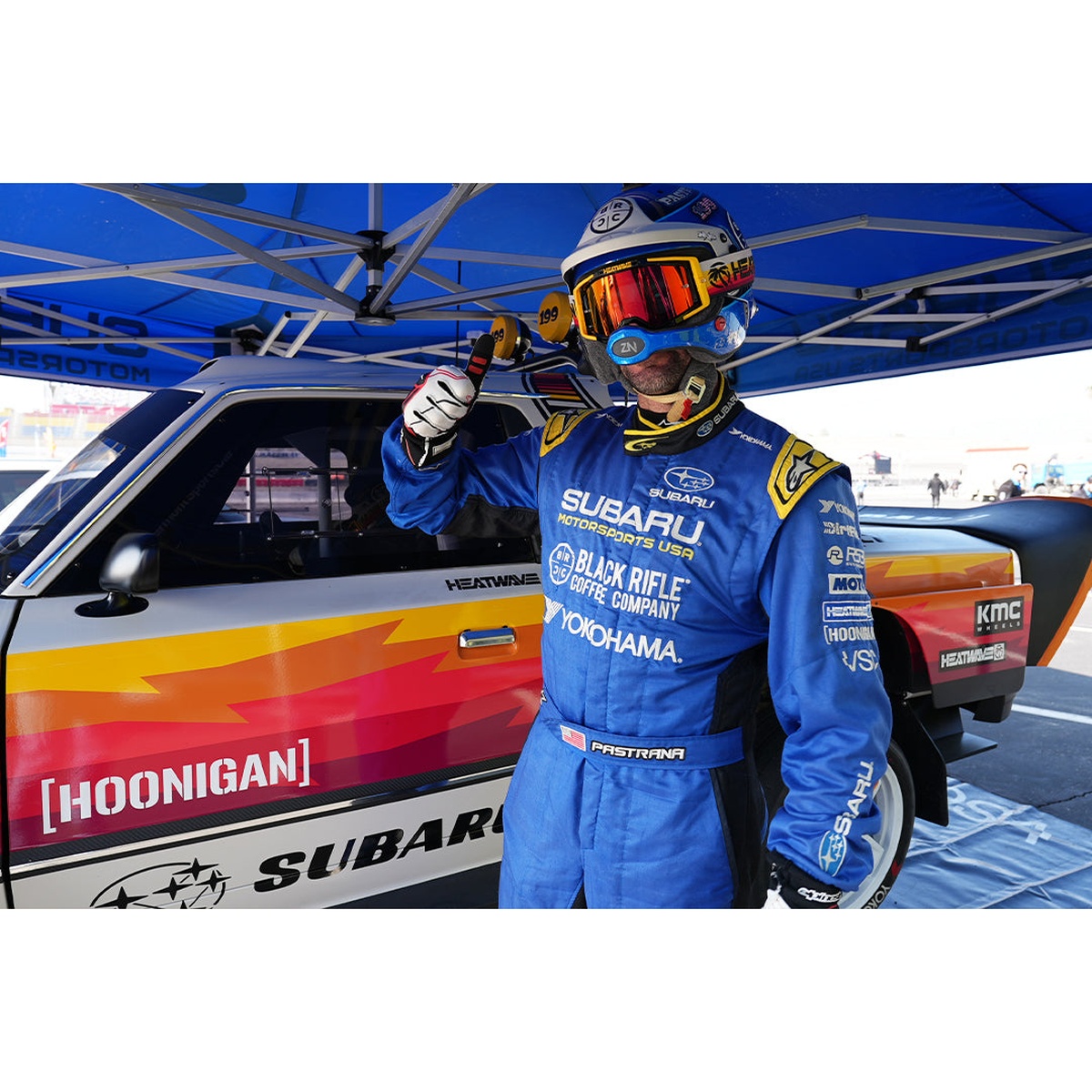 Heat Wave Visual MXG-250 Moto Goggle - Hoonigan Pastrana worn during motorsports use beside a race car in a pit environment