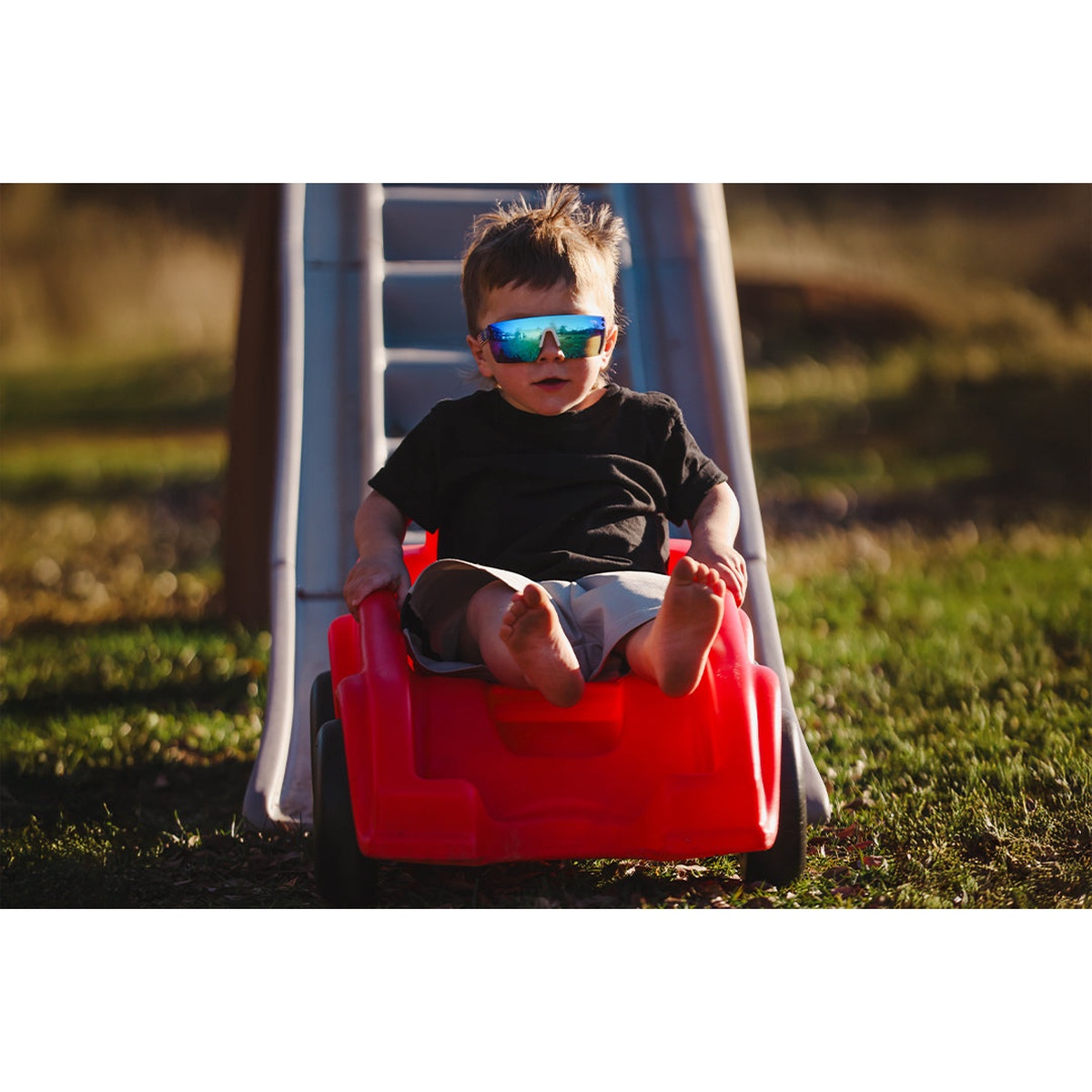 Heat Wave Visual Kids Lazer Face Sunglasses used during outdoor play on a slide in sunny backyard conditions