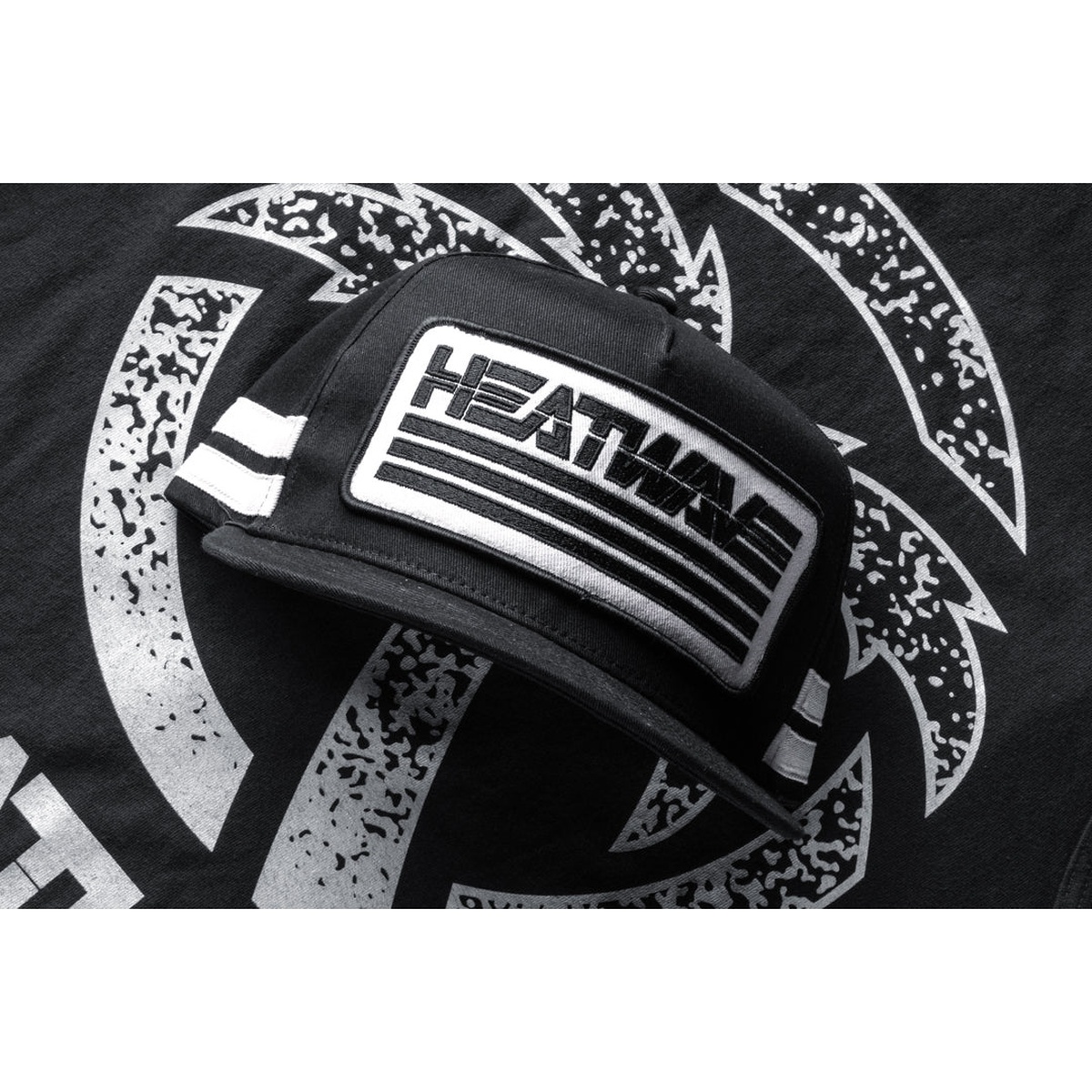 Heatwave Alloy Hat laid flat showing oversized front patch and black silver trucker-inspired design