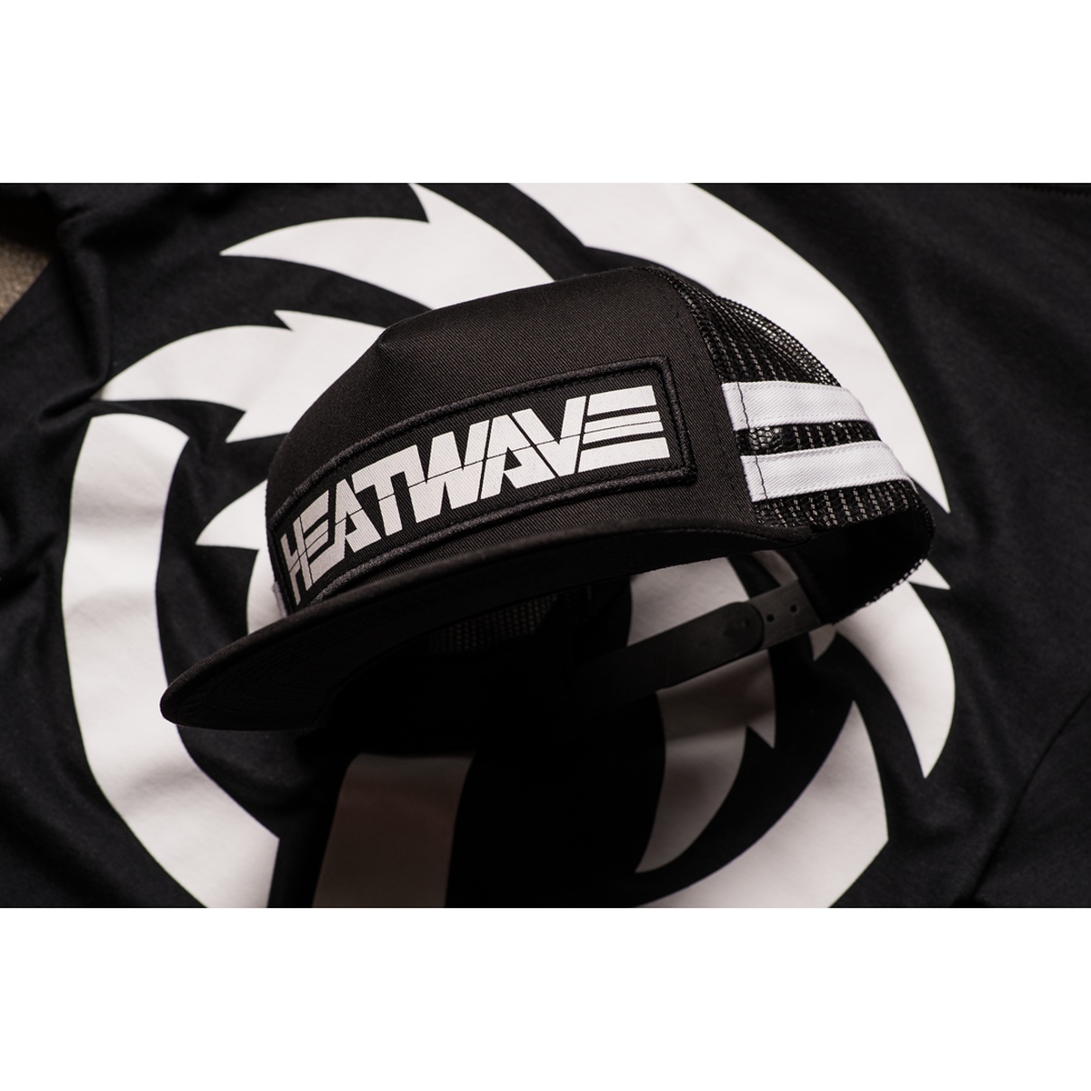 Heat Wave Visual HWV Billboard Trucker Hat lifestyle product view showing black trucker cap with mesh side panels and white stripes for warm-weather casual use