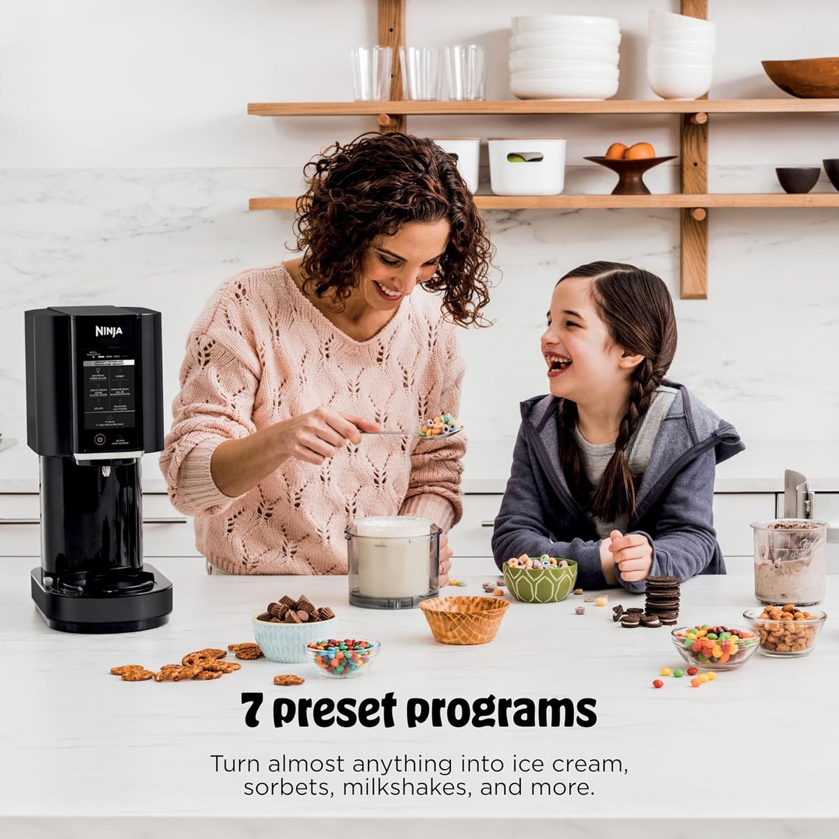 Ninja Creami on a kitchen counter with toppings and two people preparing a treat