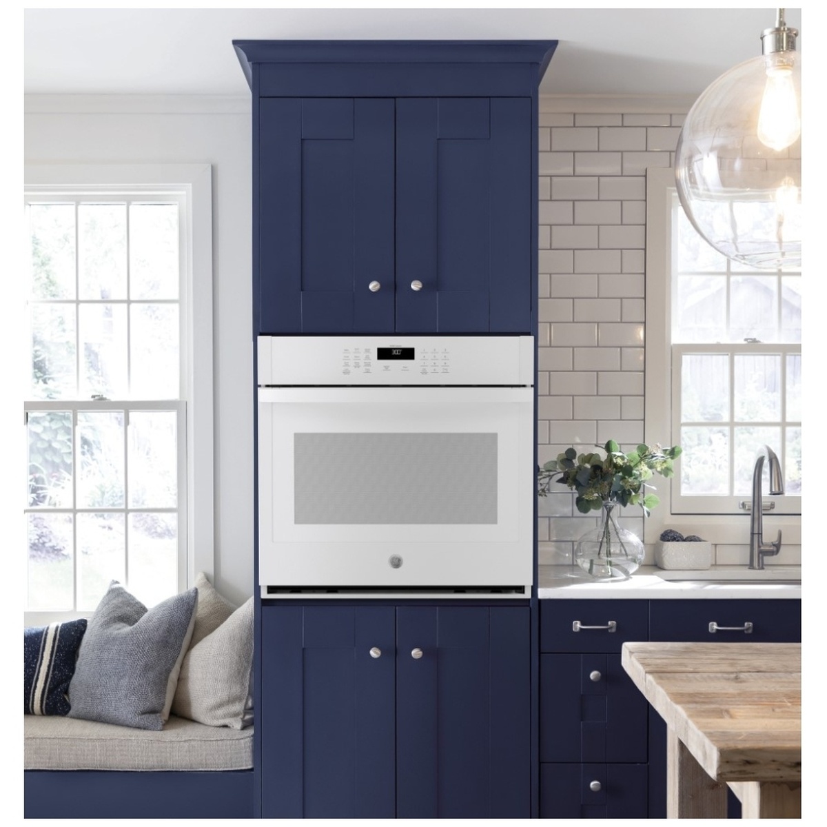 White GE wall oven installed in a navy built-in cabinet kitchen.
