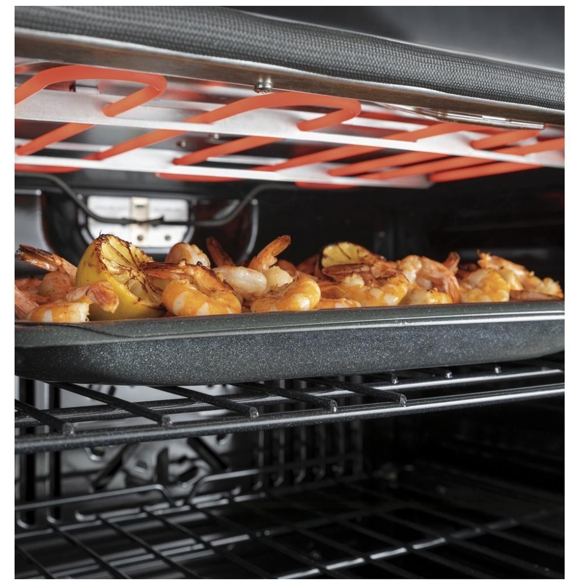 Broil element glowing red above a pan of shrimp and lemon for even browning.