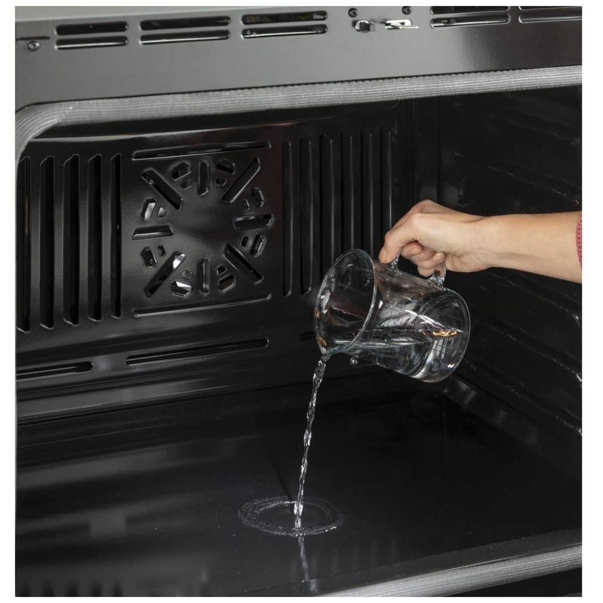 Hand pouring water into the oven floor to start a steam clean.