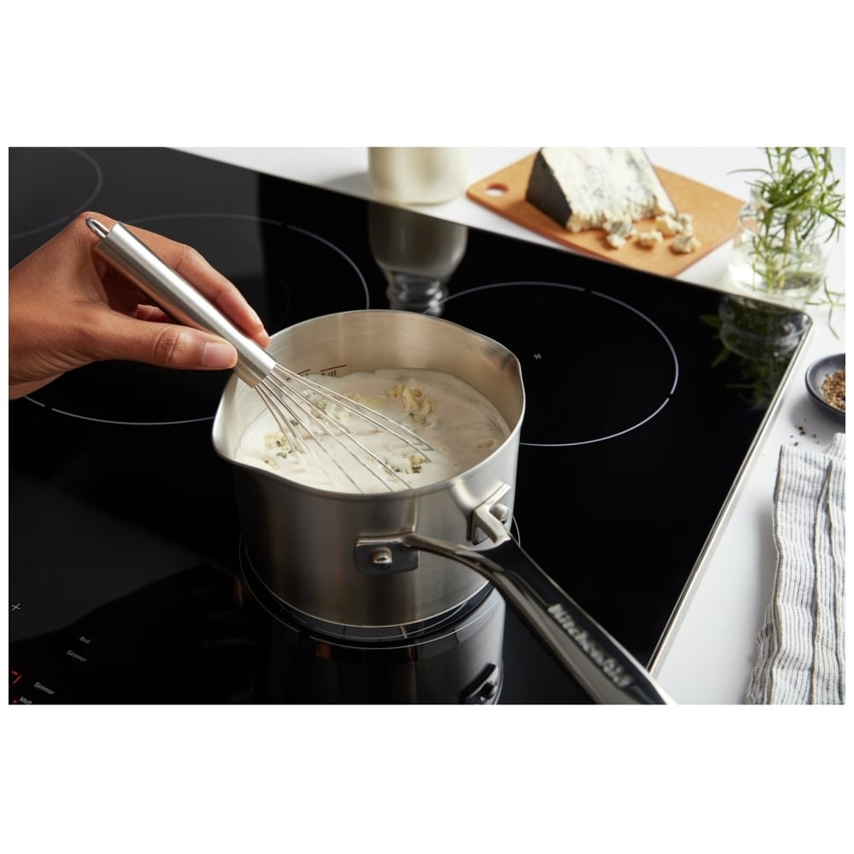 Cooktop in use with a saucepan and whisk gently simmering a creamy sauce.