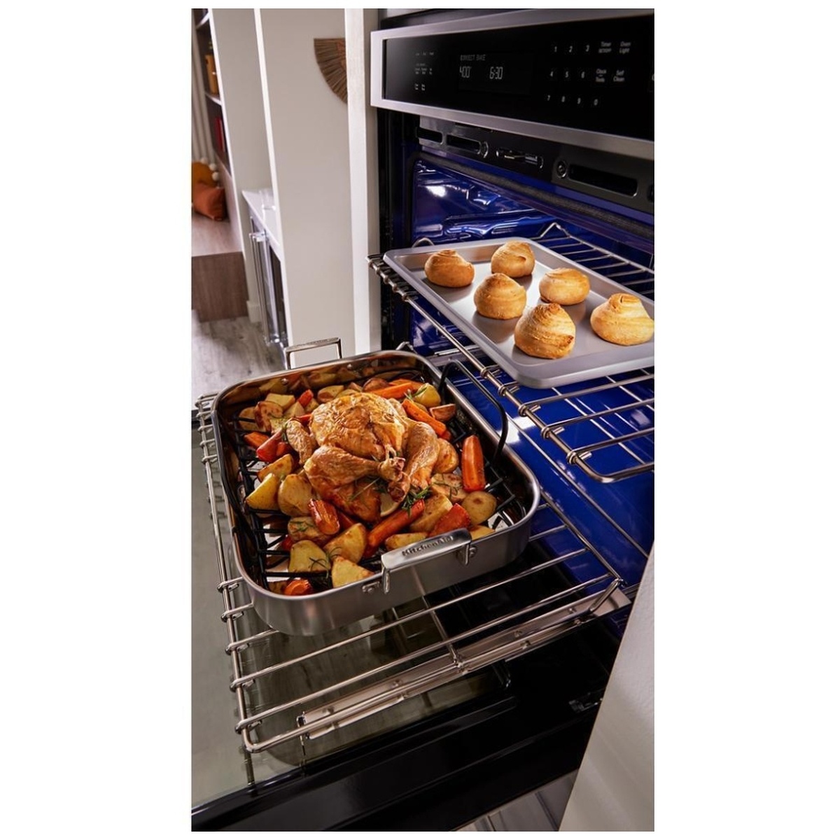 Roll-out rack extended with a heavy roasting pan and a tray of baked rolls inside the oven.