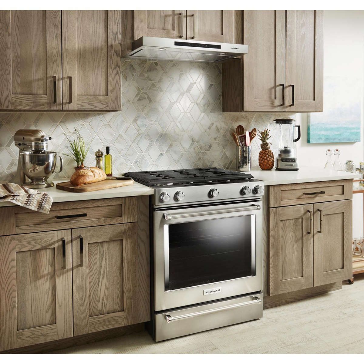 Installed KitchenAid low-profile hood illuminating a gas range in a modern kitchen.