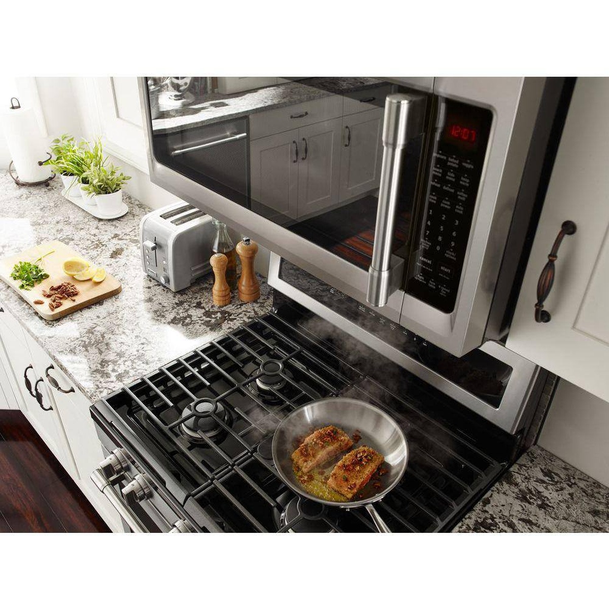 Range hood capturing steam rising from a pan on a gas cooktop in a bright kitchen.