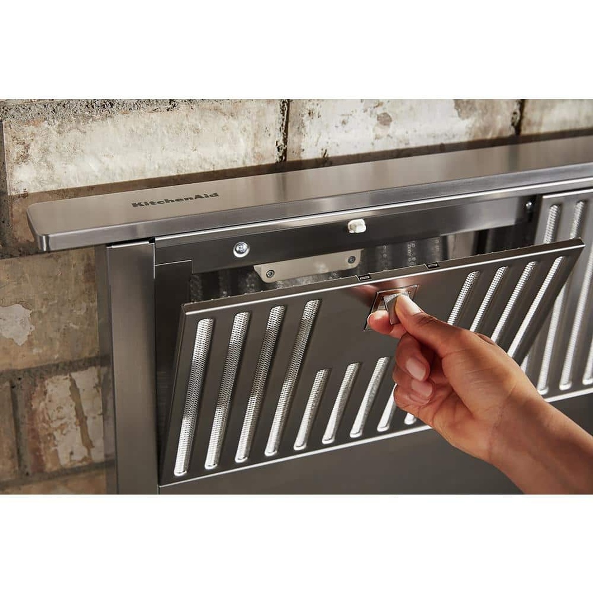 Hand removing the stainless grease filter from the downdraft vent.