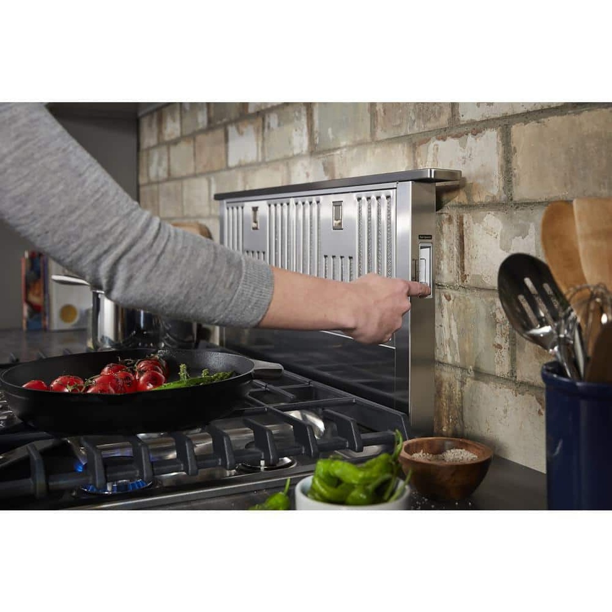User activating the downdraft vent beside a gas cooktop.
