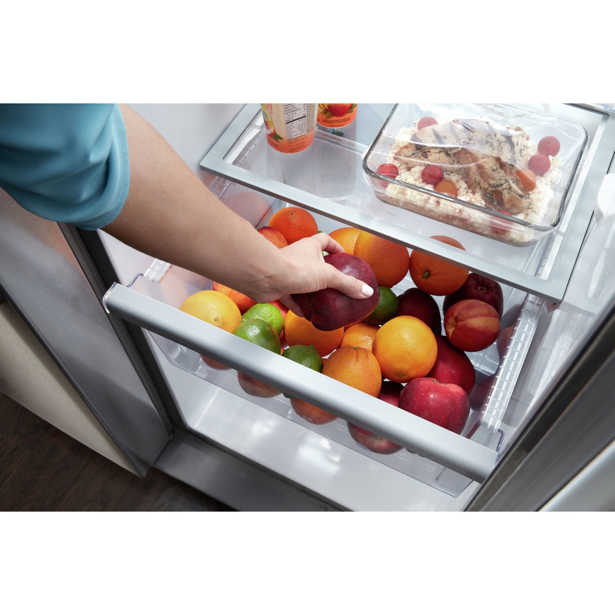 Hand accessing the humidity-controlled crisper drawer filled with fresh produce