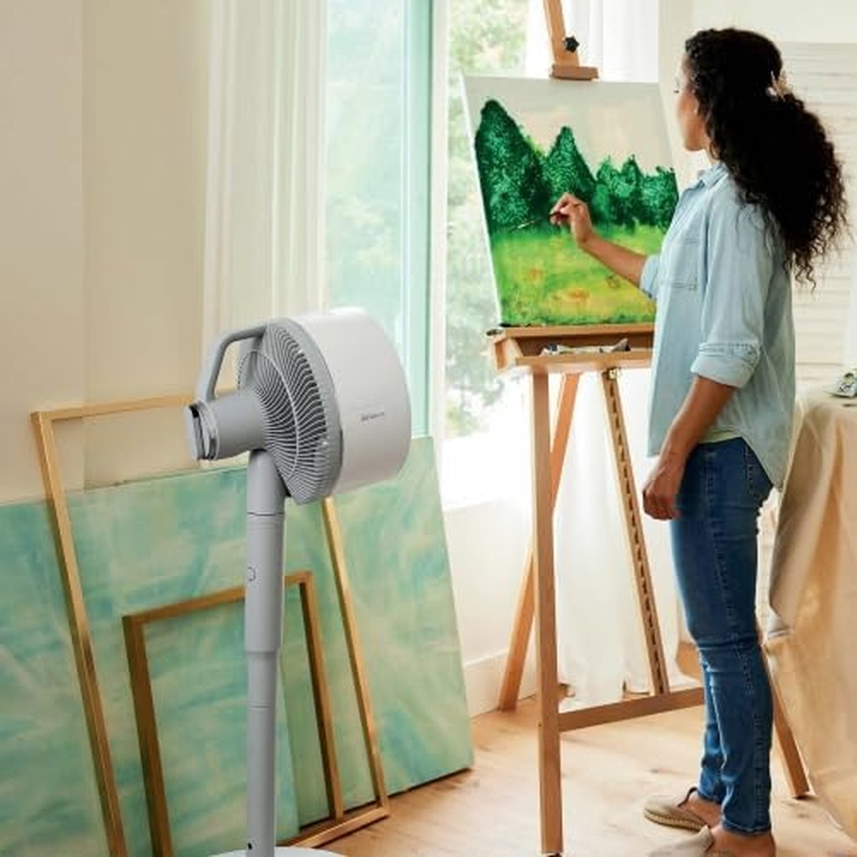 Pedestal fan cooling an artist in a bright studio