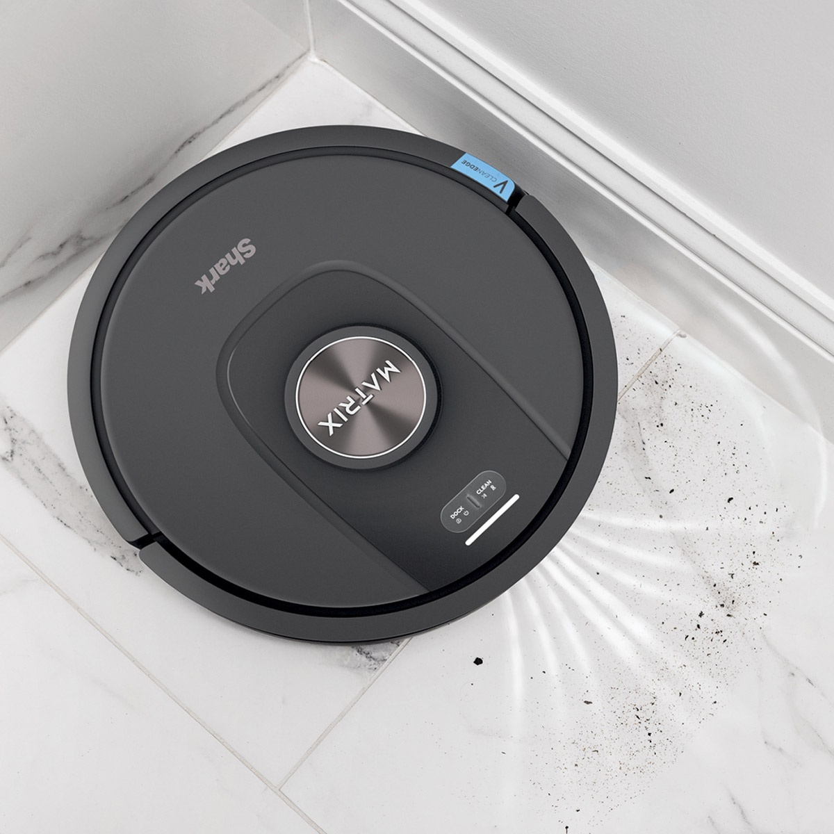 Robot vacuum cleaning debris along a wall and corner on tile flooring